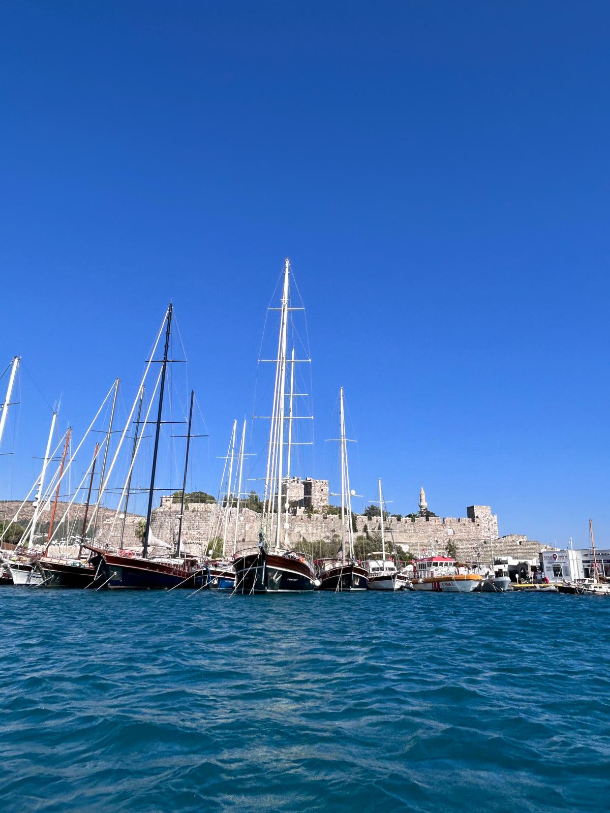 Mavi deniz ve gökyüzü önünde Bodrum Kalesi ile limandaki guletler