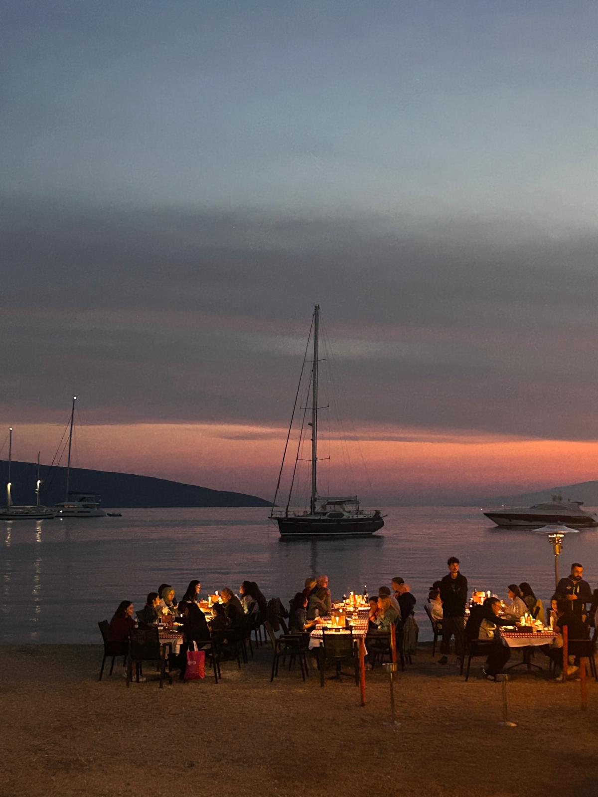 Bodrum sahilinde günbatımında deniz kenarında yemek yiyen insanlar ve tekneler